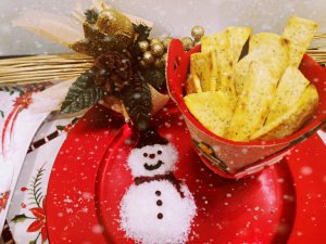Crackers alla curcuma con semi di papavero nel piatto rosso con decorazione a pupazzo di neve fatta con il sale da cucina